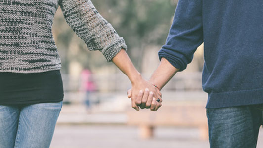 couple wearing jeans holding hands in middle of park