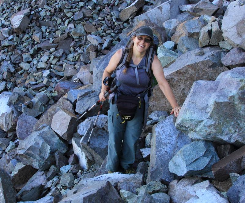 Female hiker leaning on boulders with hiking poles and backpack